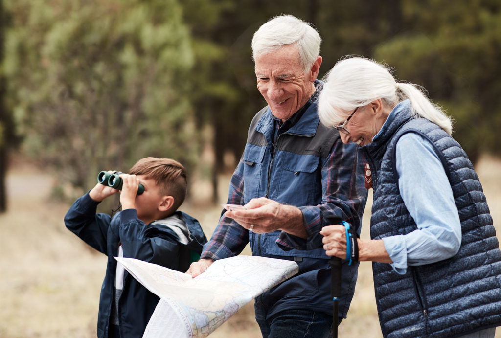 Grandparents looking at a compass and map while a young boy looks through binoculars on a nature walk