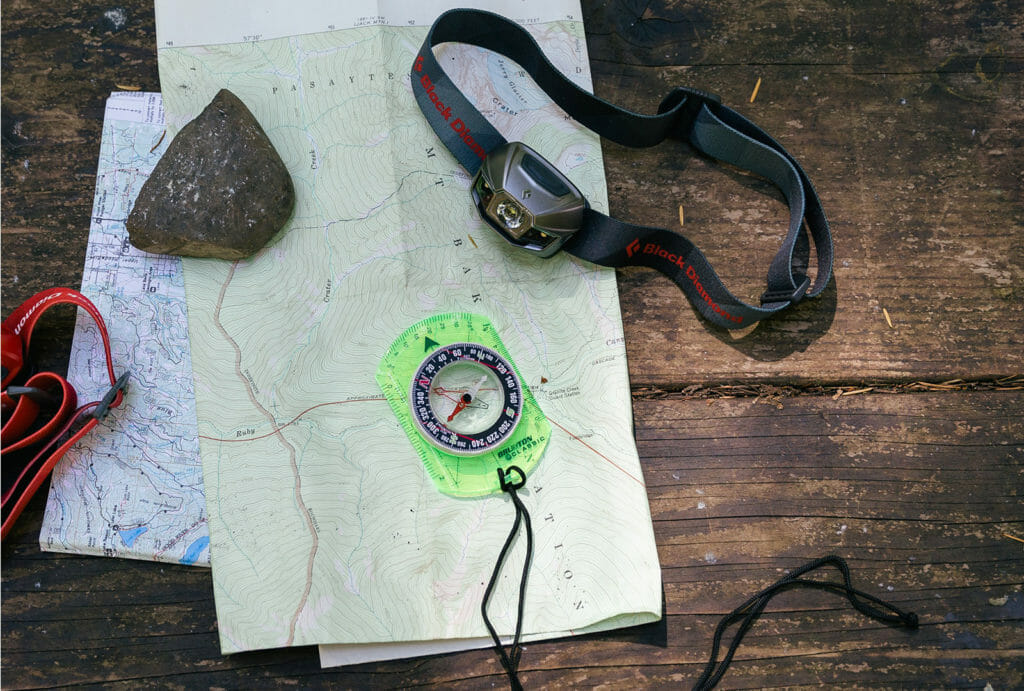 Map, compass, and headlamp laying on wood table