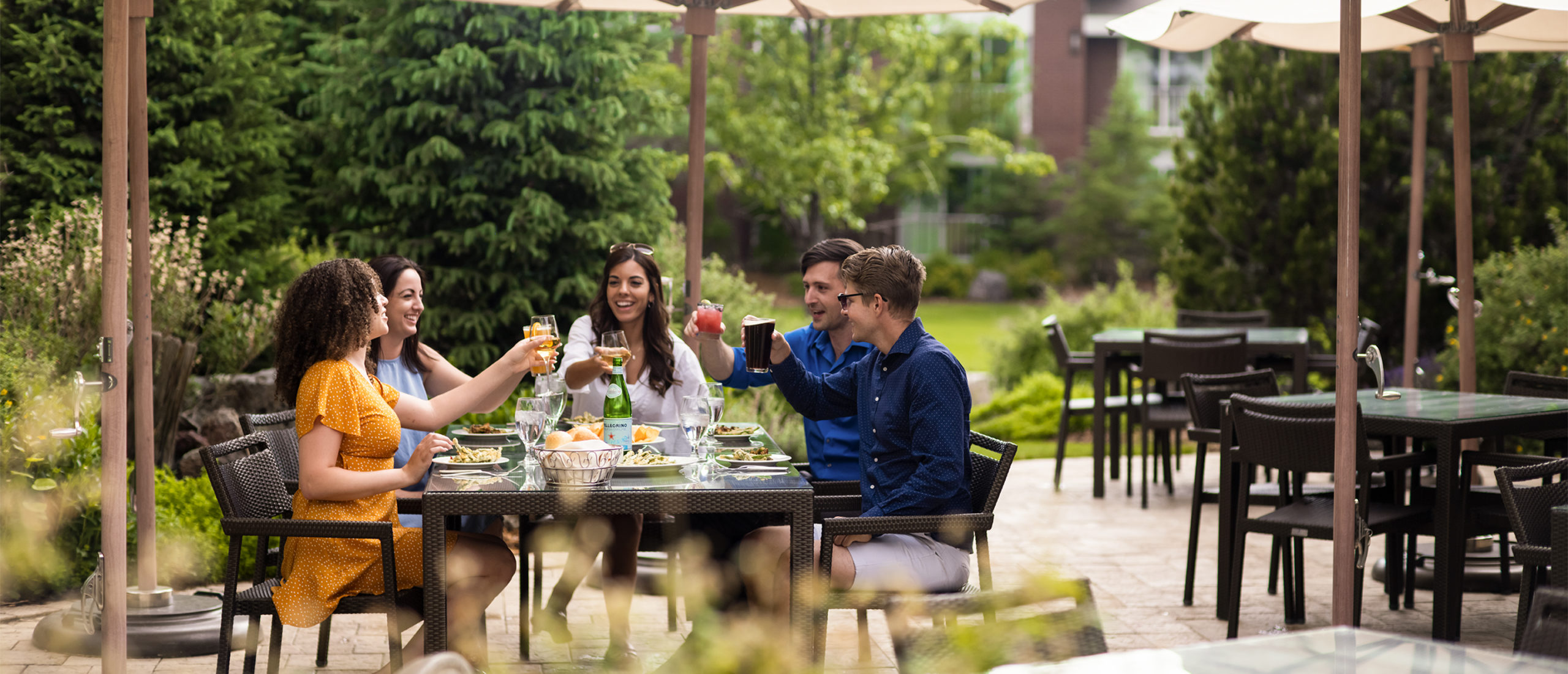 A group of five friends raising glasses at a table on Silver Pine Restaurant's outdoor patio.