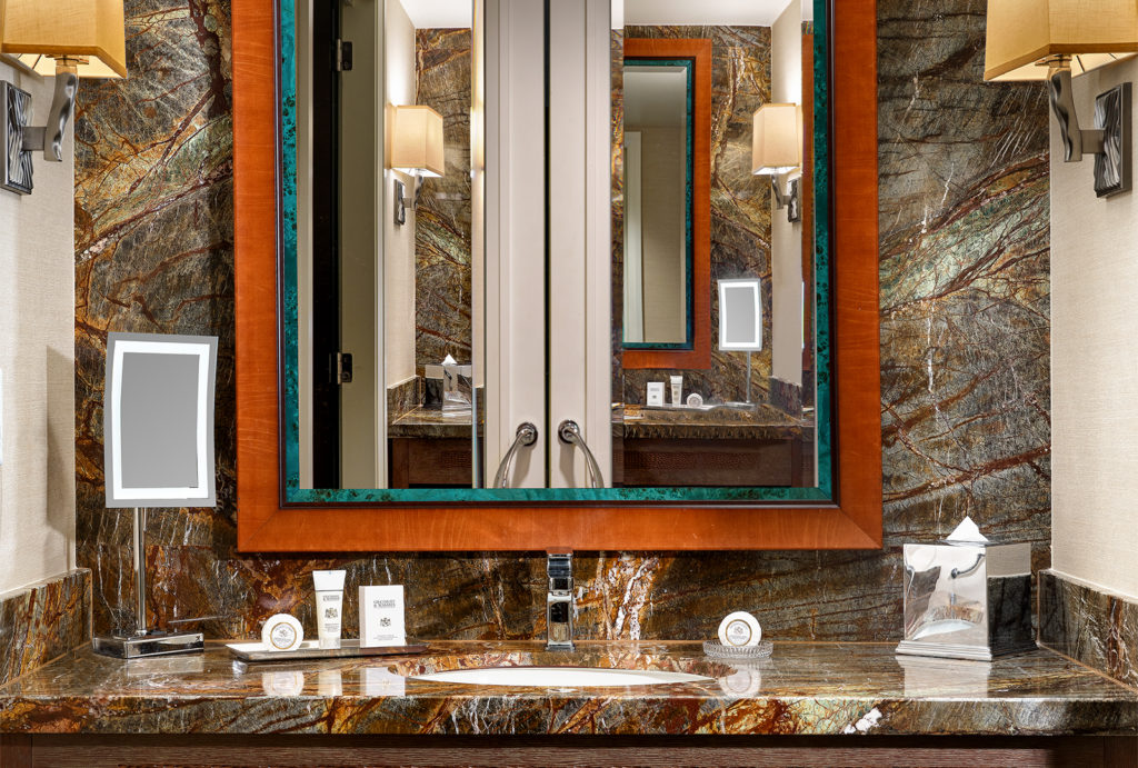 Close up of bathroom sink with a mirror reflecting the double doors behind it.
