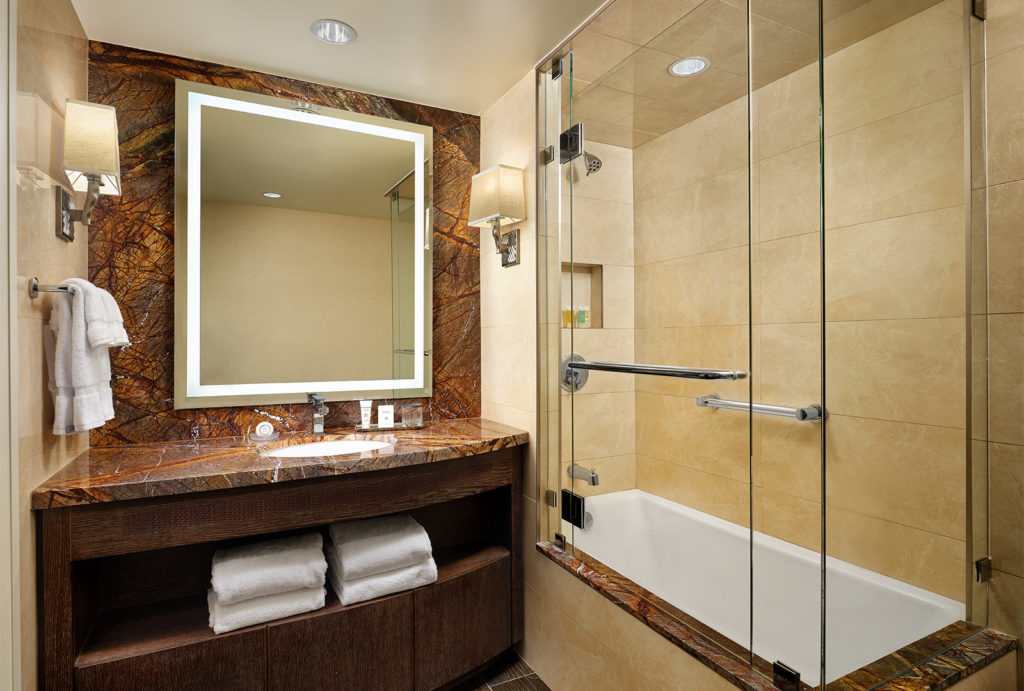 Bathroom sink with backlit mirror next to the large shower and bathtub area.