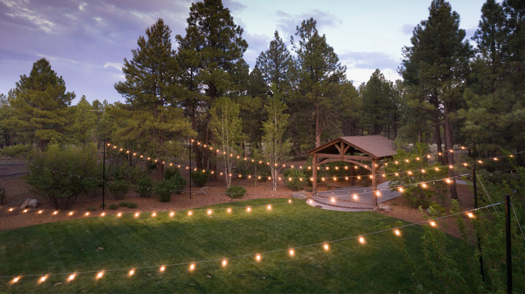 Little America Flagstaff lawn area with lights strung across with many pine trees in the background.