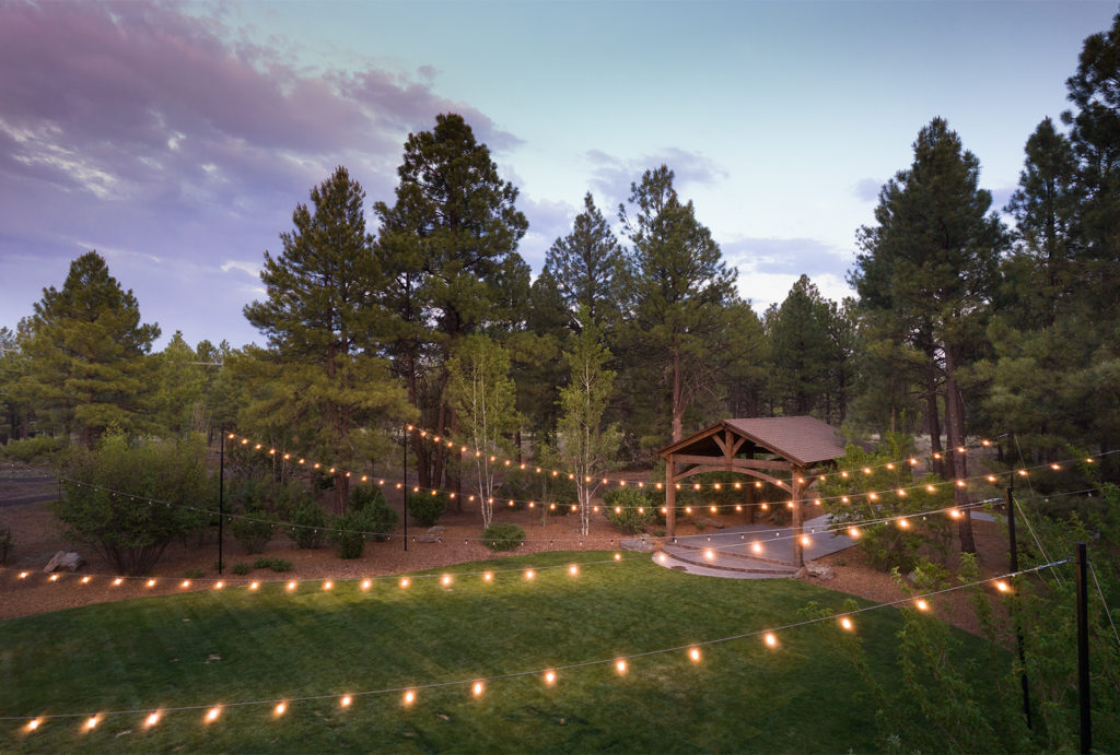 Little America Flagstaff lawn area with lights strung across with many pine trees in the background.