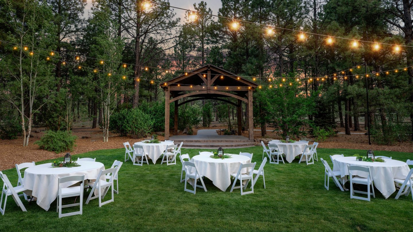 Outdoor grassy area set up with tables near the outdoor arch with lights strung across the lawn