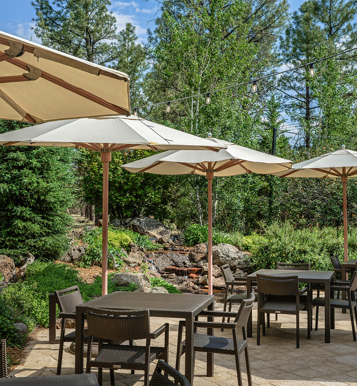 The patio at Silver Pine Restaurant with tables, chairs and umbrellas with a waterfall in the background.