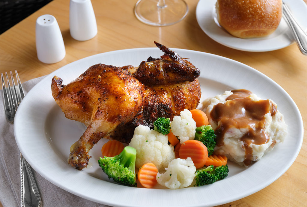 Close up of a chicken dinner with mashed potatoes and gravy with mixed vegetables.