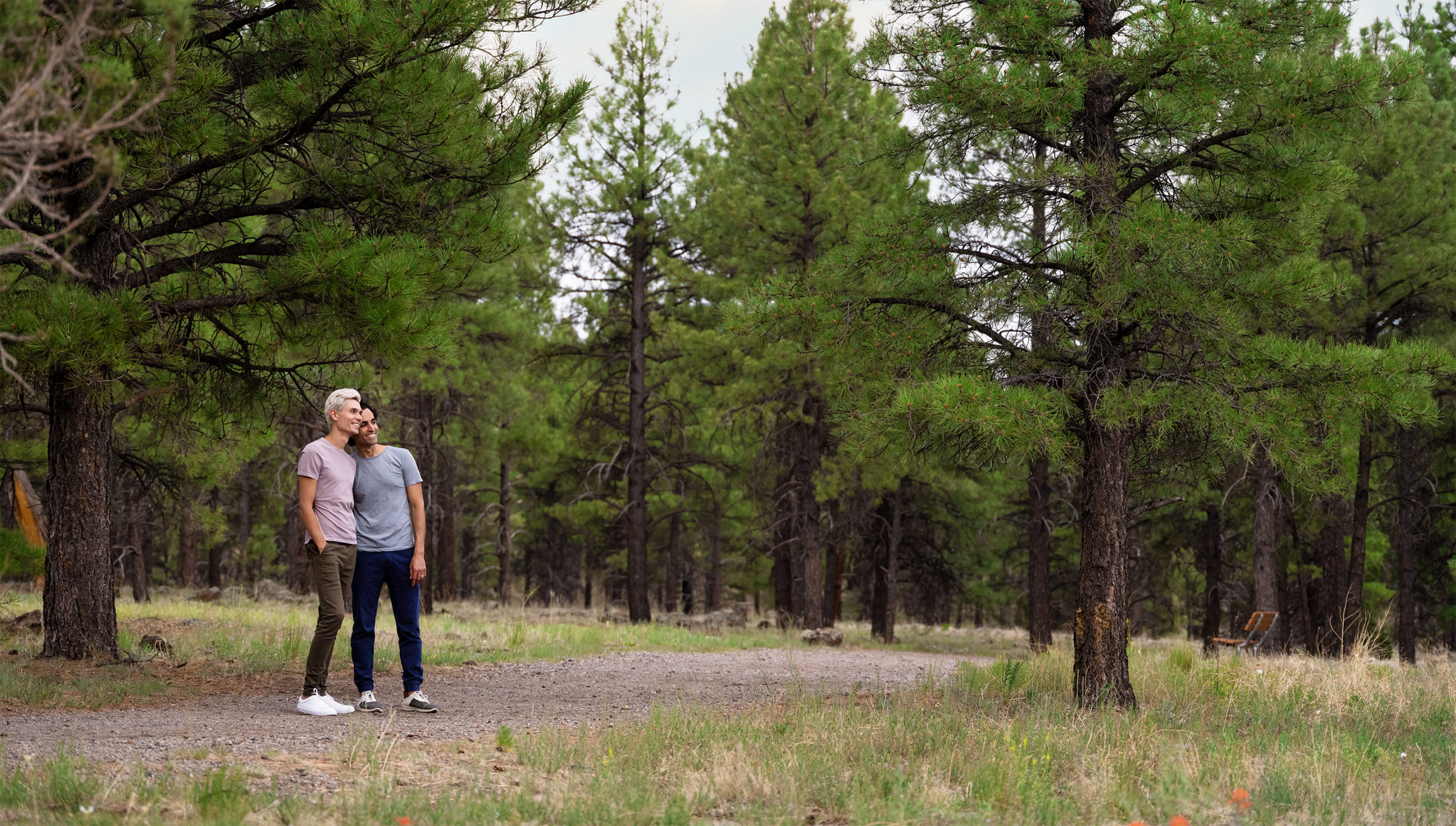 A couple standing on a trail with pine trees in the background.