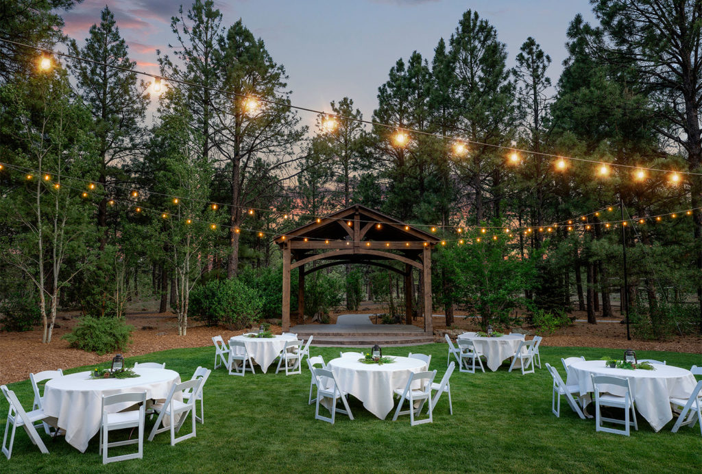 Outdoor grassy area set up with tables near the outdoor arch with lights strung across the lawn