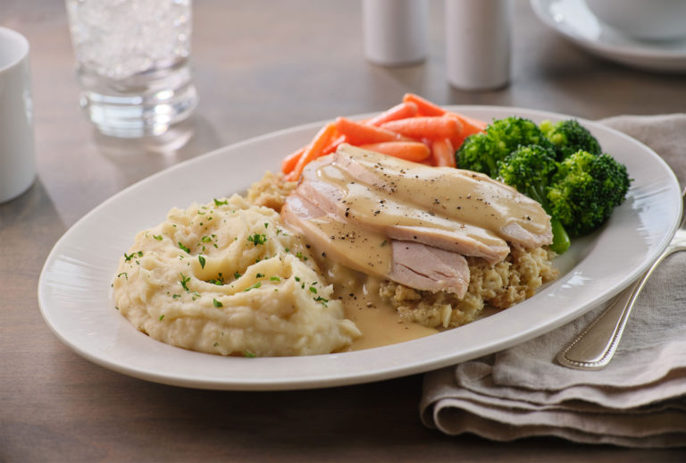 Close up of a plate of turkey, mashed potatoes, stuffing, and vegetables.